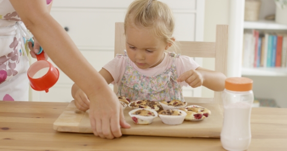 Woman Placing Tray Of Muffins In Front Of Child