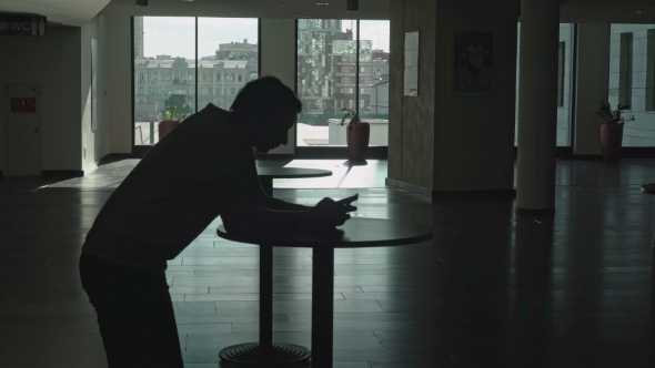 The Figure Of a Young Man Leaning On a Table In The Lobby Of The Room And Holding a Phone.