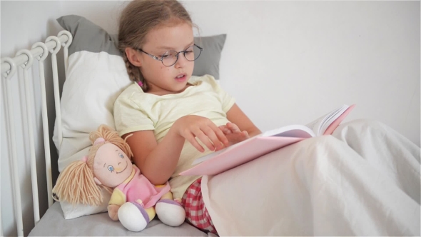 Little Girl With Glasses Leafing Through a Book While Lying In Bed. Perhaps a Child Is Sick
