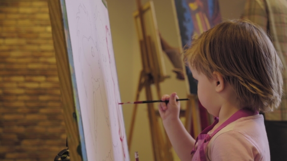 The Little Girl In a Pink Shirt Paints Paints On Canvas.