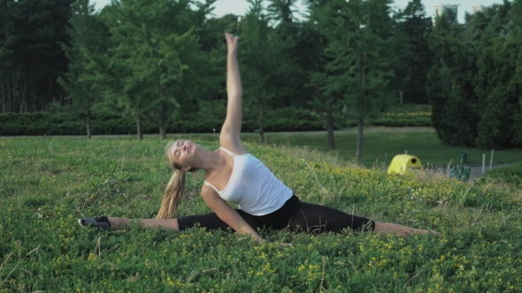 Young Slender Blonde In Shirt Performs Exercise Incline On The Hill With Green Grass In The Park.