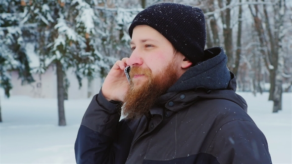 Attractive Young Bearded Man Talking on the Phone. It Goes in the Winter Park