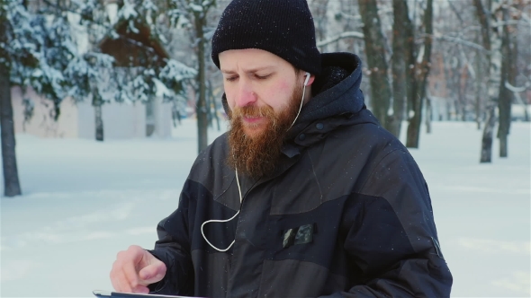 Steadicam Shot: Attractive Bearded Man Walking In a Winter Park, Enjoys a Tablet