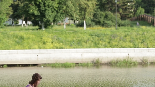 Young Woman Write Something In Her Notebook On River Bank In City Park