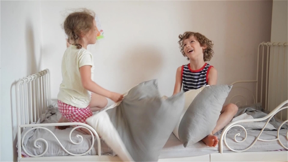The Brother And The Sister Have Arranged Fight By Pillows On a Bed In a Bedroom. The Naughty Little