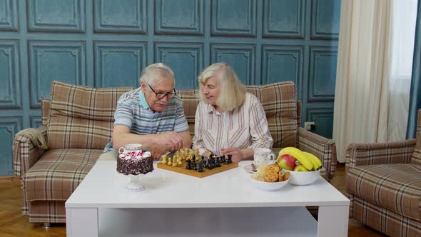 Retired Senior Couple Talking Drinking Tea Playing Chess in Modern Living Home Room Lounge Together