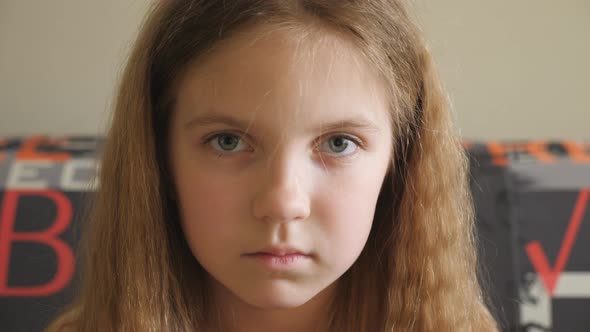 Small Disappointed Kid Sitting on the Couch and Looking Into Camera. Portrait of Unhappy Little Girl