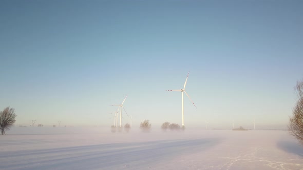 Wind Turbines On Snowy Field In Poland Standing Against Blue Sky Background With Propeller Rotating.