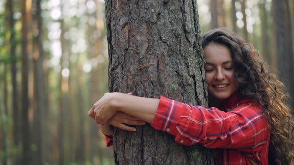 Beautiful Young Woman with Curly Hair Wearing Bright Shirt Is Hugging Tree Enjoying Nature and