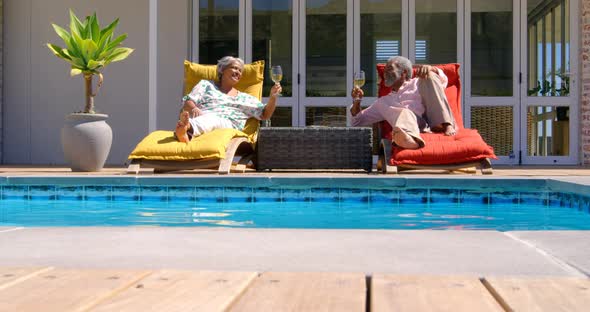 Front view of black senior couple relaxing on pool deck chair in back yard of their home 4k