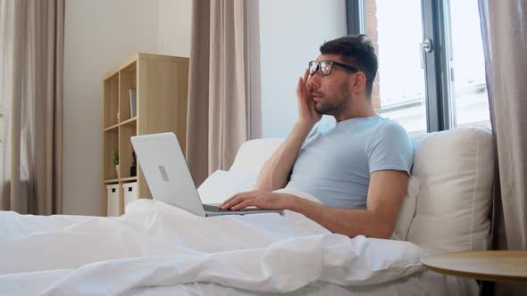 Tired Man in Glasses with Laptop Working in Bed