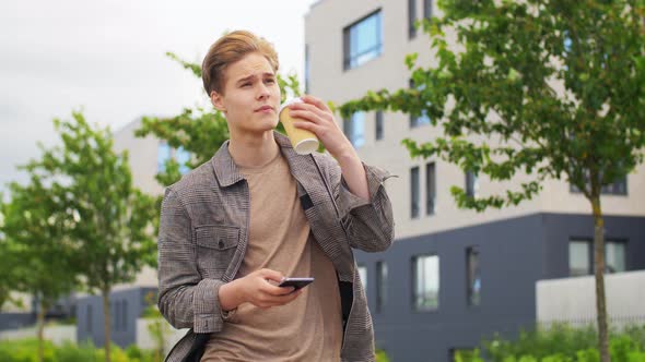 Young Man with Smartphone Drinking Coffee in City