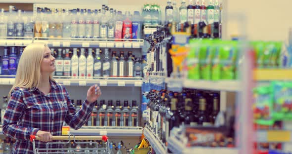 Woman Shopping for Wine or Other Alcohol in a Bottle Store Standing in Front of Shelves Full of