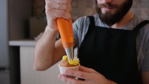 A Pastry Chef in the Kitchen Decorating a Cupcake with Whipped Cream or Cheese Cream