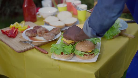 Unrecognizable African American Man Making Delicious Meat Burgers on Table for Picnic