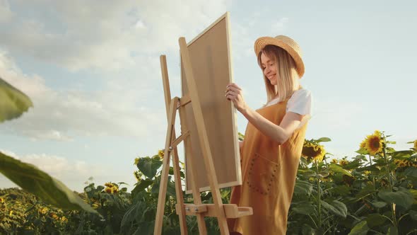 A Young Woman is Putting the Painting on an Easel