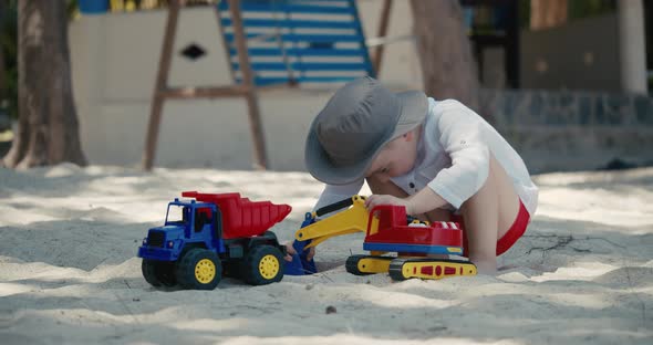 Children Plays with a Plastic Car in the Sand on the Beach