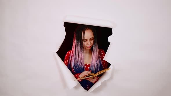 Young Woman Reading Book in Hole of White Background in Studio