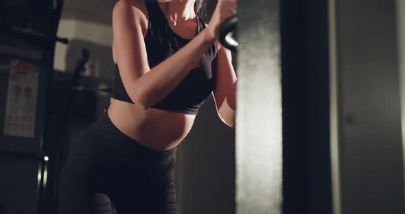 Concentrated Female Athlete Pulls Bar with Rope and Weights on Simulator in Gym