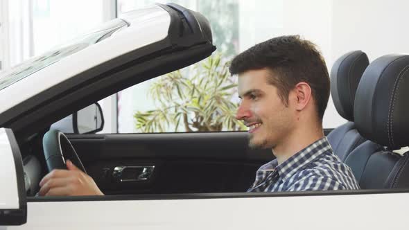 Happy Young Handsome Man Sitting in a New Convertible at the Dealership