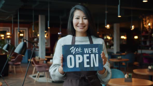 Portrait of Beautiful Asian Businesswoman in Apron Holding Open Sign in Modern Cafe