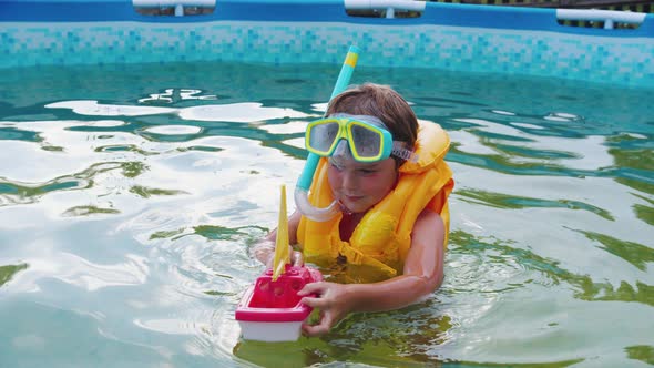 A Little Boy in Underwater Mask Playing with a Toy Boat in the Swimming Pool