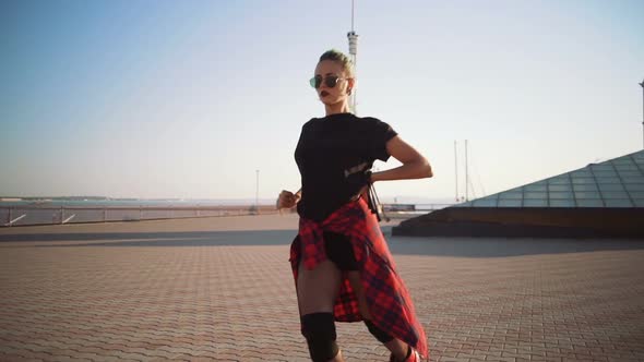 Young Stylish Funky Girl with Green Hair Riding Roller Skates and Dancing Near Sea Port During