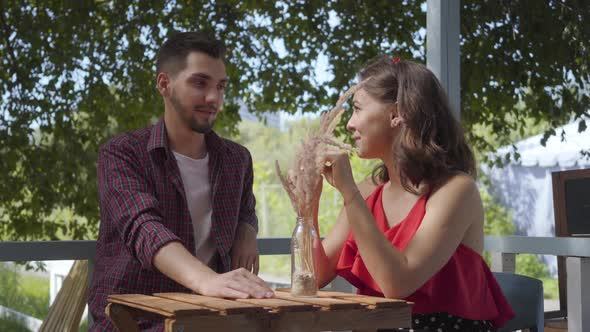 Young Happy Couple Sitting Outdoors at the Small Table Talking and Smiling To Each Other