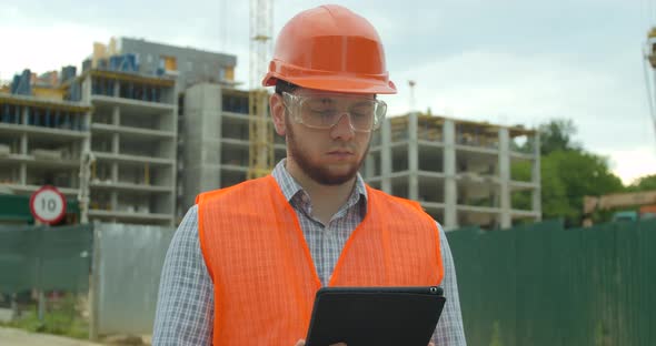 Young Architect or Builder Man Standing with Digital Touchpad on the Construction Site and Analyzing