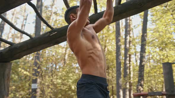 Sporty man with muscular body exercising on the horizontal ladder in the forest gym, outdoors