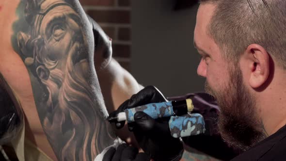 Rear View Shot of a Tattoist Making Tattoos on the Arm of Male Client