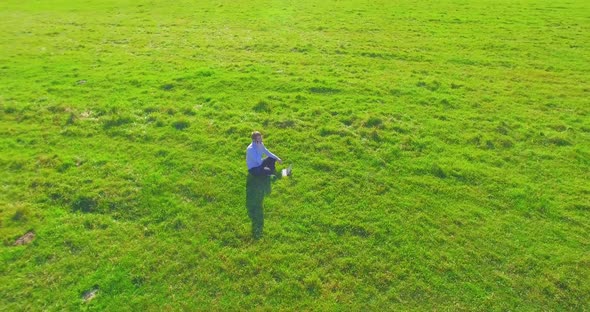 Low Orbital Flight Around Man on Green Grass with Notebook Pad at Yellow Rural Field.