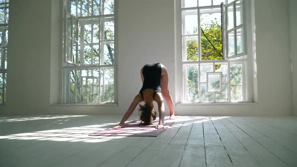 Red-haired Young Healthy Caucasian Woman Standing on the Mat in the White Large Room Practicing Yoga