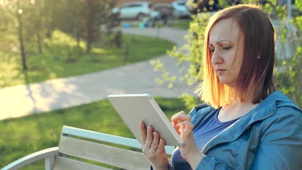 Woman Using Tablet Computer Sitting on Bench in City