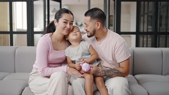 Happy Parents Sit on Grey Couch Hugging Adorable Daughter