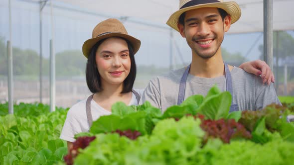 Asian couple farmers owner working in hydroponic green house farm with happiness and look at camera.