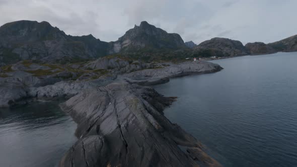 Flying over rocks at shore of Nusfjord, Lofoten looking at Nusfjord and mountains in the background