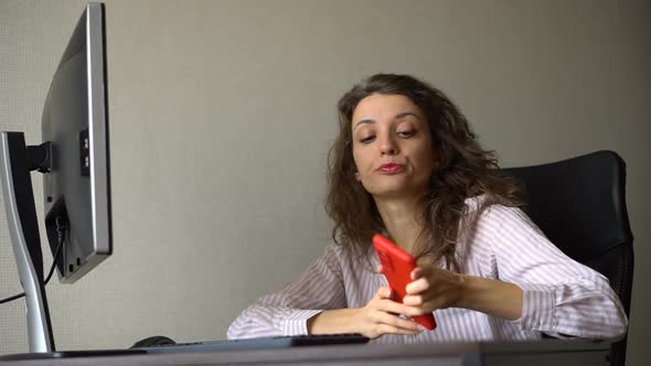 Tired Young Woman with Curly Hair and White Shirt is Working at the Office and Using Her Red