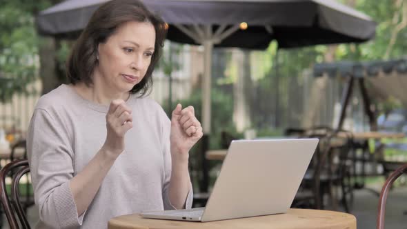 Upset Old Woman Reacting to Loss on Laptop Sitting Outdoor