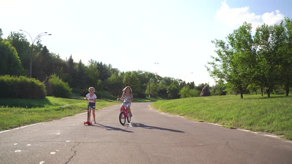 Front View Two Girls Riding Scooter And Bike On Driveway