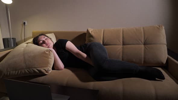 Young Woman Lies on Brown Sofa with Large Pillows and Sleeps