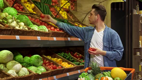 Man Takes Tomatos and Cucumber From the Rack at the Supermarket