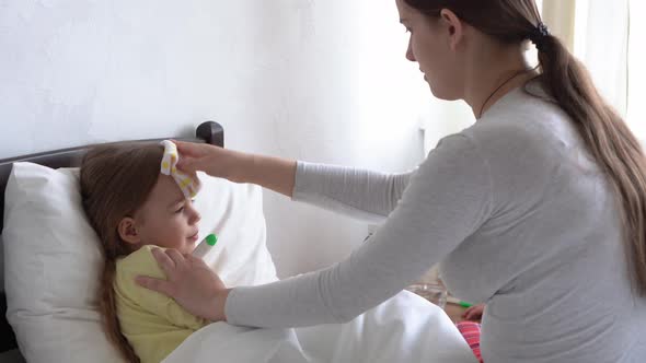 Young Caucasian Woman Nurse or Doctor Examines Baby Girl Measures Temperature with Thermometer Under