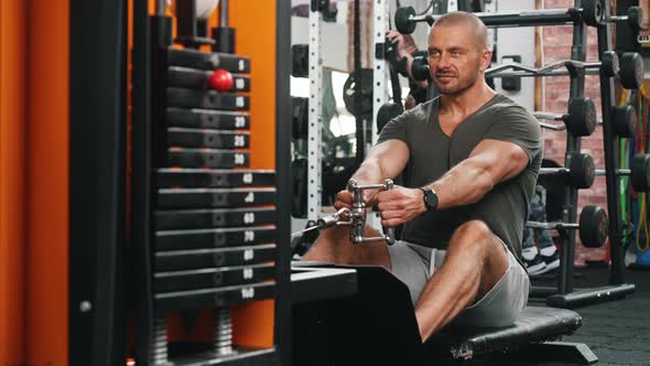 Front View of a Goodlooking Sexy Middleaged Guy with a Beard Doing Exercise on a Rowing Machine in a