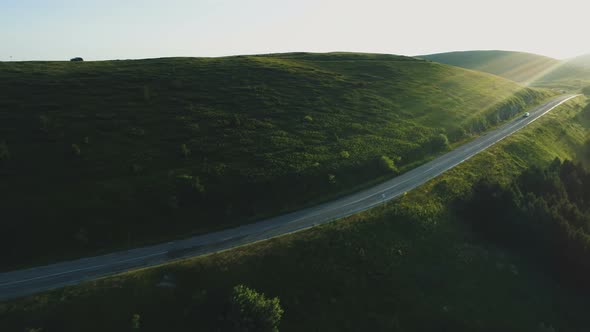 Aerial View of Black Car Driving on Beautiful Mountain Road with Green Hills at Sunset