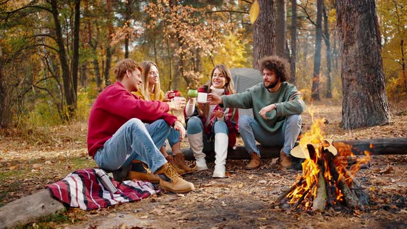 Friends Laughing Cheering with Cups Sitting on Log in Autumn Forest