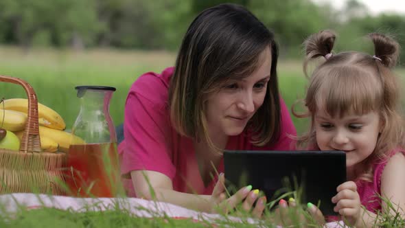 Family Weekend Picnic. Daughter Child Girl with Mother Play Online Games on Tablet. Chatting