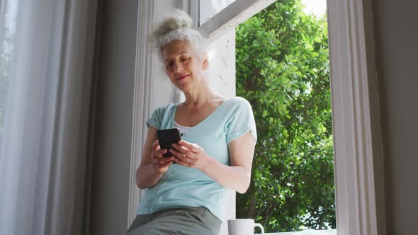 Senior caucasian woman using smartphone near the window at home