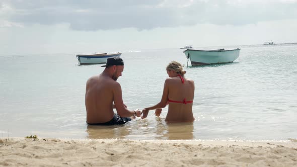 Caucasian young couple relaxing and resting on shore and sandy beach during sunlight. Travel trip in