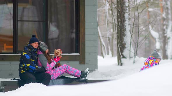 Man Hugs Wife with Dog While Daughter Plays with Snow